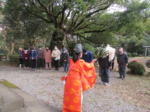 境内で複数の年配の男女が横一列に並んで巫女さんにお祓いを受けている様子の写真