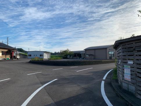 白い白線で間隔的に引かれた道路が右側に大きくカーブしており、その道中に建物も複数立ち並んでいる写真