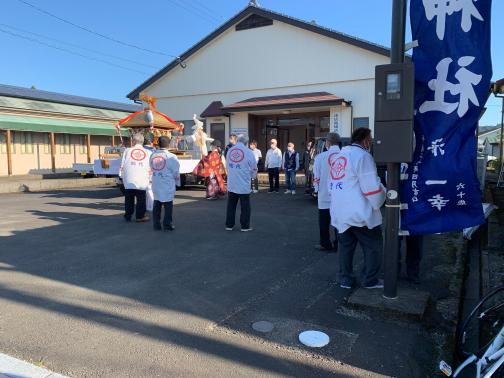 公民館の前で複数の男性と神主が神事を行っている写真