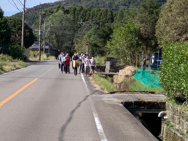 森の前の道路を複数の男女が太鼓を叩きながら歩いている写真