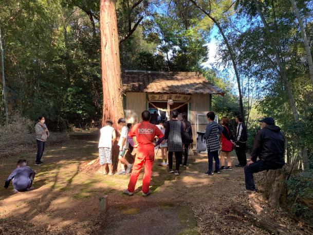 複数の男女が小さな神社の前に集まっている写真