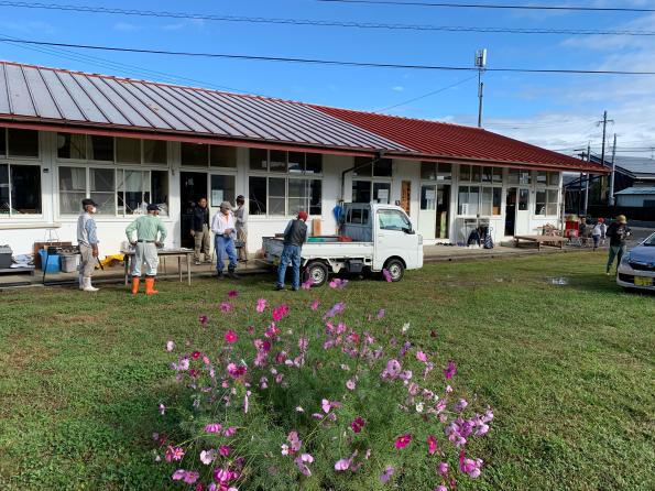 平屋の窓が複数ある建物の前に一台の軽自動車と人がいる写真