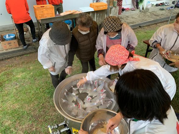 女性6名が鍋に決まった量の水と米を入れた袋を沸騰させている様子の写真