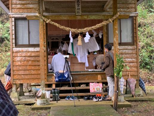 しめ縄が吊り下げられている神社の中で男性2人と神主が奉納している写真