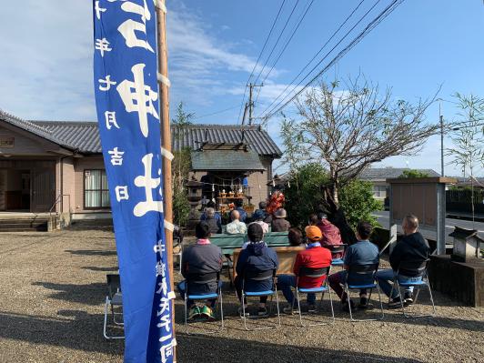 青いのぼりが手前に掲げられてその奥に住民の皆さんが本尊に集まっている様子が写っている写真