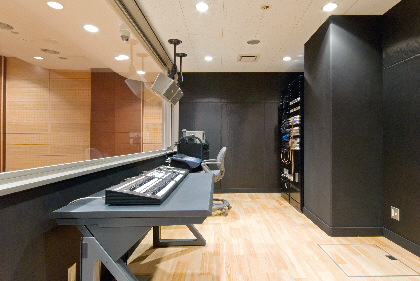 木の床と黒い壁のある部屋に置かれた机の上に、キーボードのような音楽機材がある写真